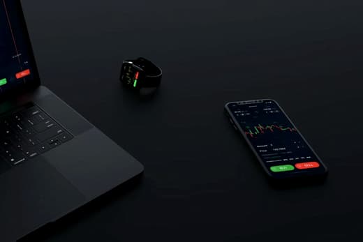 A laptop and phone showing financial charts on a dark desk